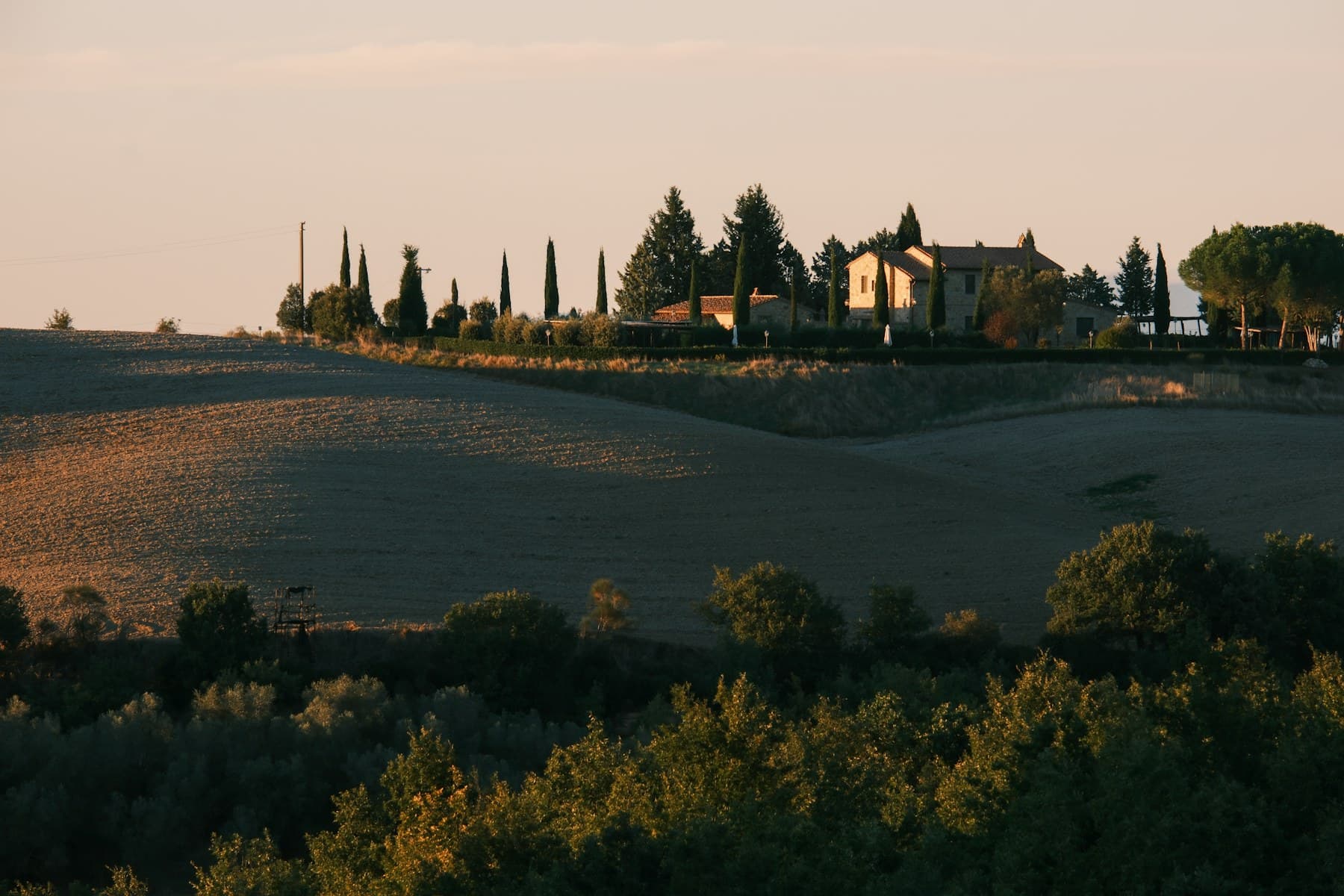 Casale nella campagna toscana con colline morbide e luce calda del tramonto
